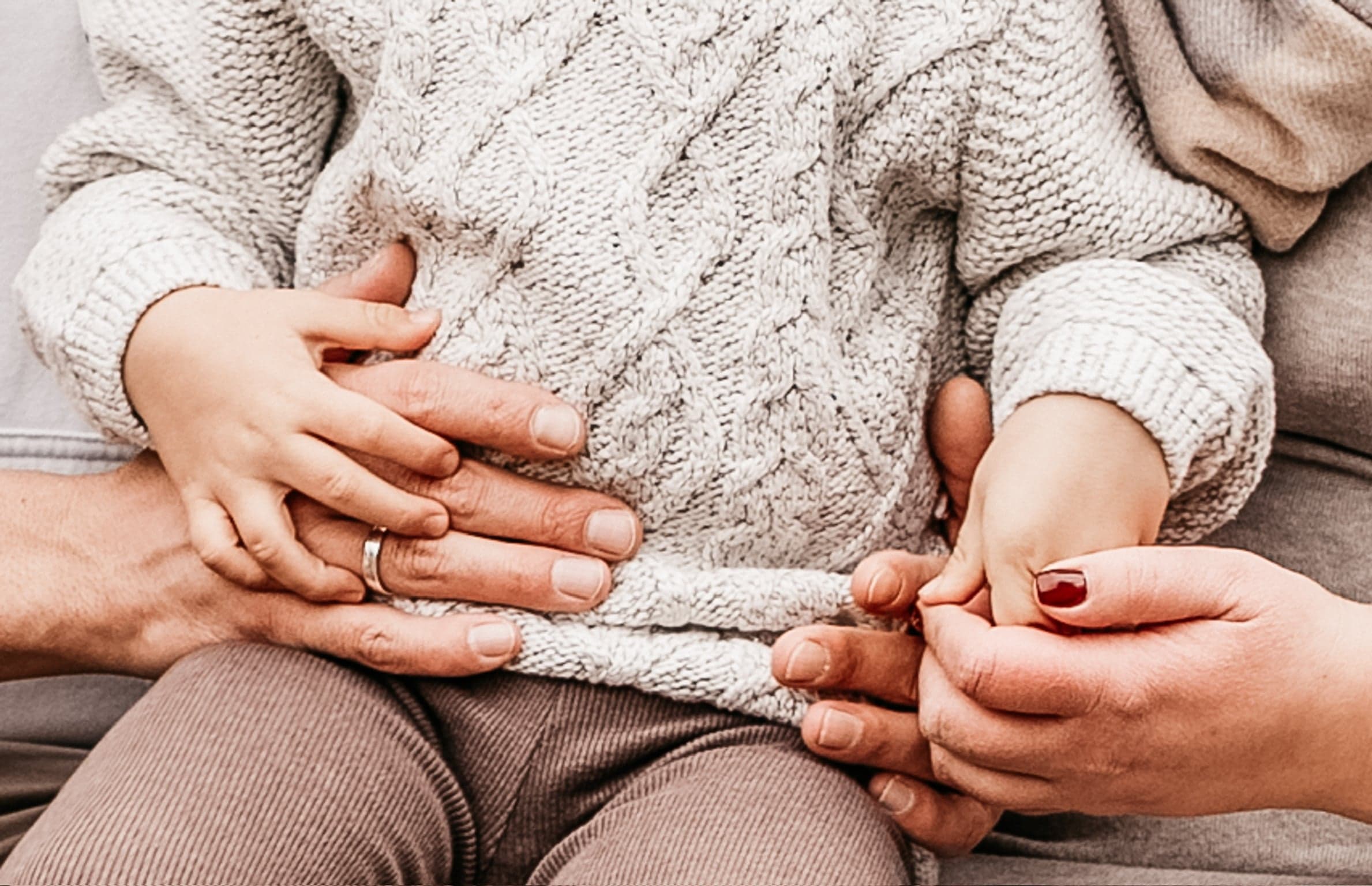 Hände von Eltern und Kind übereinander auf einem Strickpullover