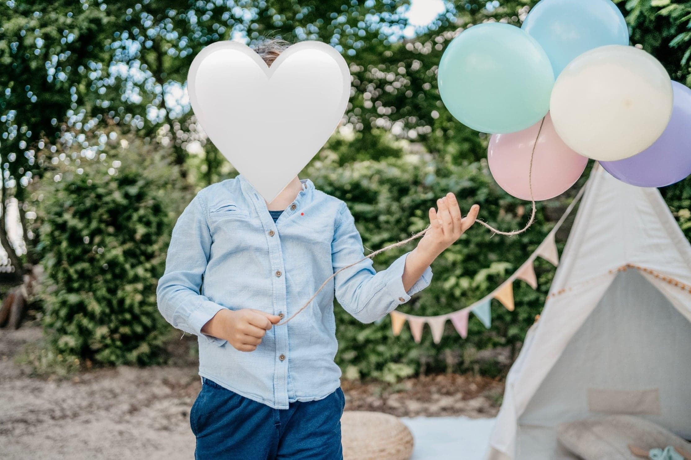 Junge im Hemd mit Luftballons neben einem Tipi im Garten