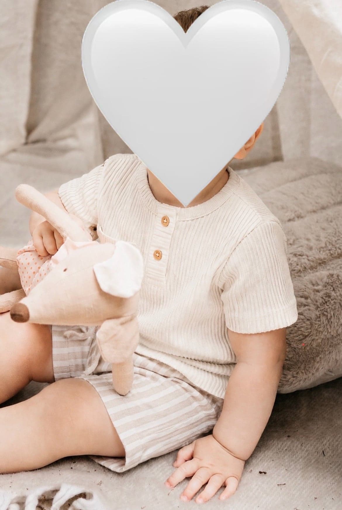 Kleinkind sitzt mit Kuscheltier auf einer Decke