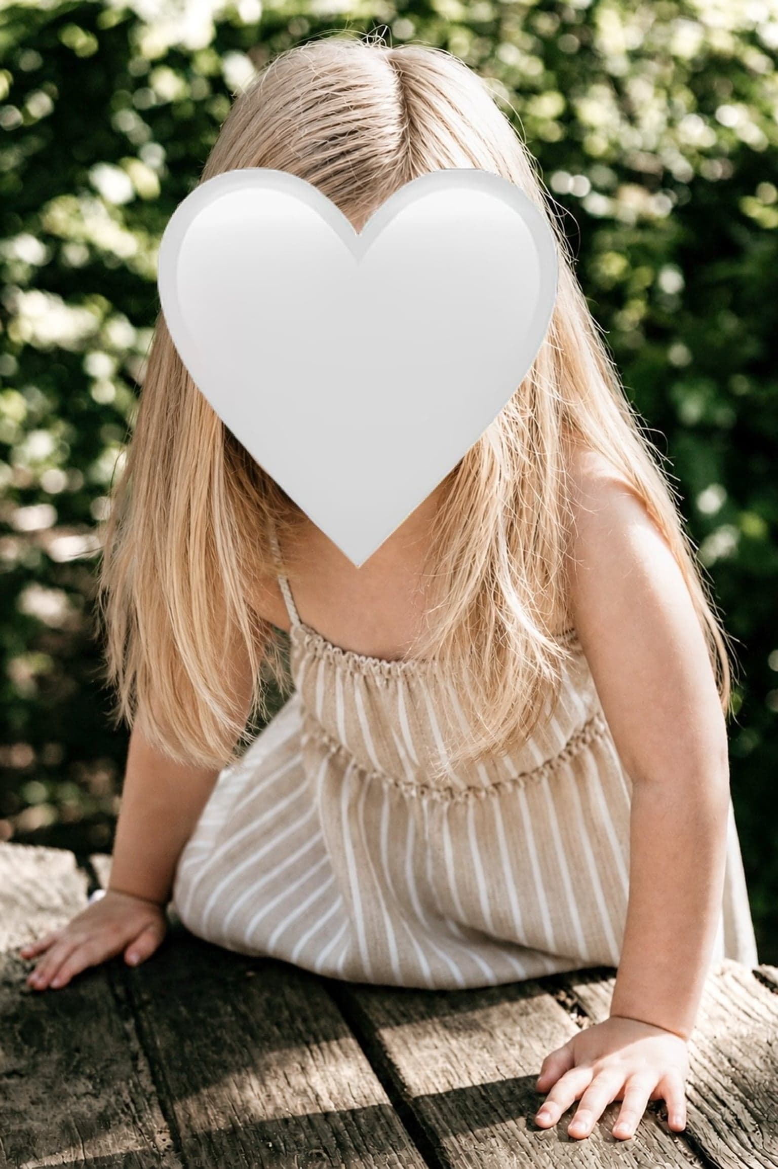 Mädchen im Sommerkleid stützt sich auf einen Holztisch im Garten